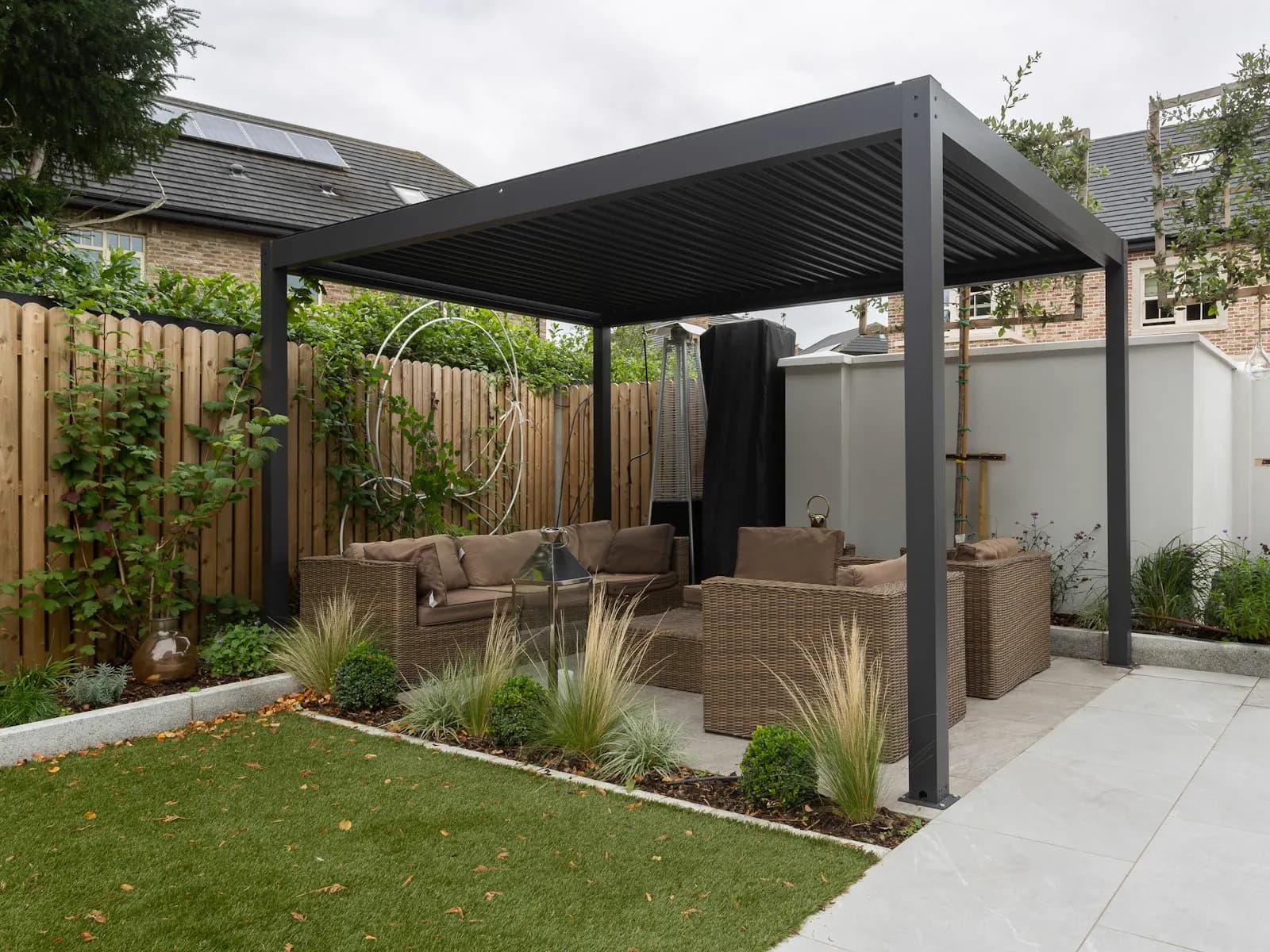 Pergola bioclimatica antracite su un patio con salotto da esterno e giardino